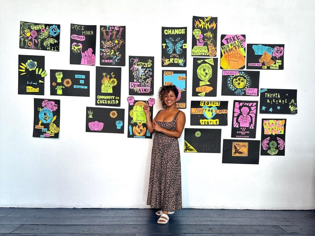 Favianna stands in front of a wall of student-made climate justice posters